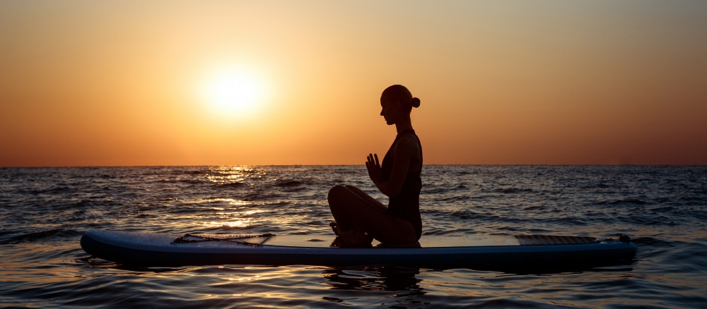 Woman meditating by the sea at sunset