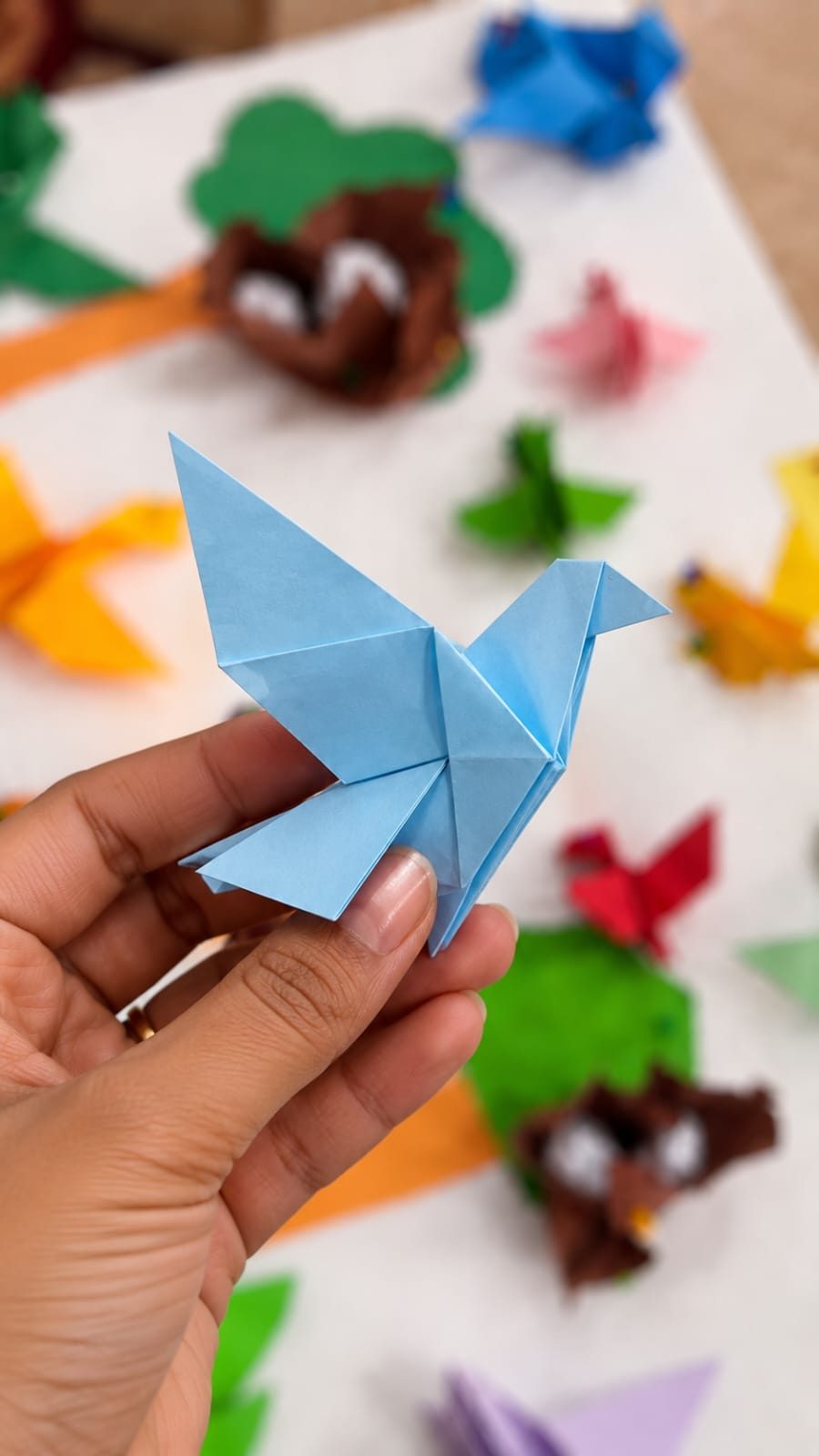 Hand holding an origami bird among colourful paper birds